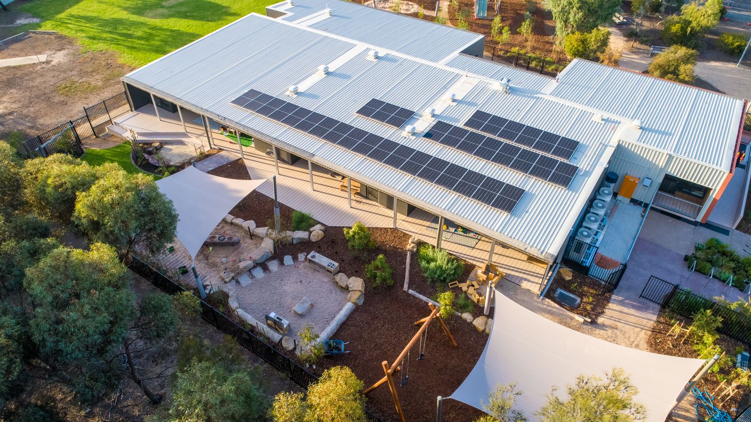 Angled aerial view of Early Learning Victoria Bani Walup (Murtoa) showing solar-panelled roof, outdoor play areas, shade sails and surrounding gum trees.