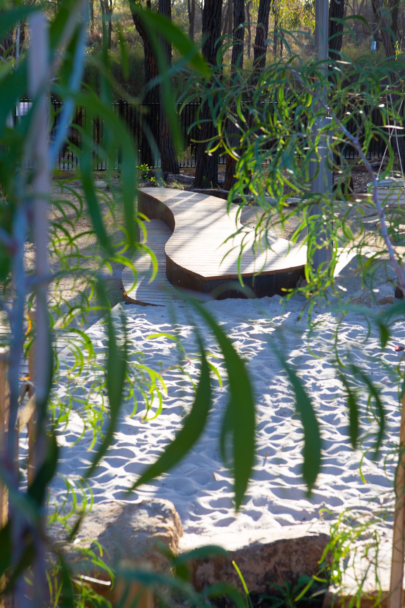 Outdoor play space at Early Learning Victoria Nyernilang Lar (Eaglehawk North) with sandpit and curved wooden seating, framed by blurred foliage in foreground.